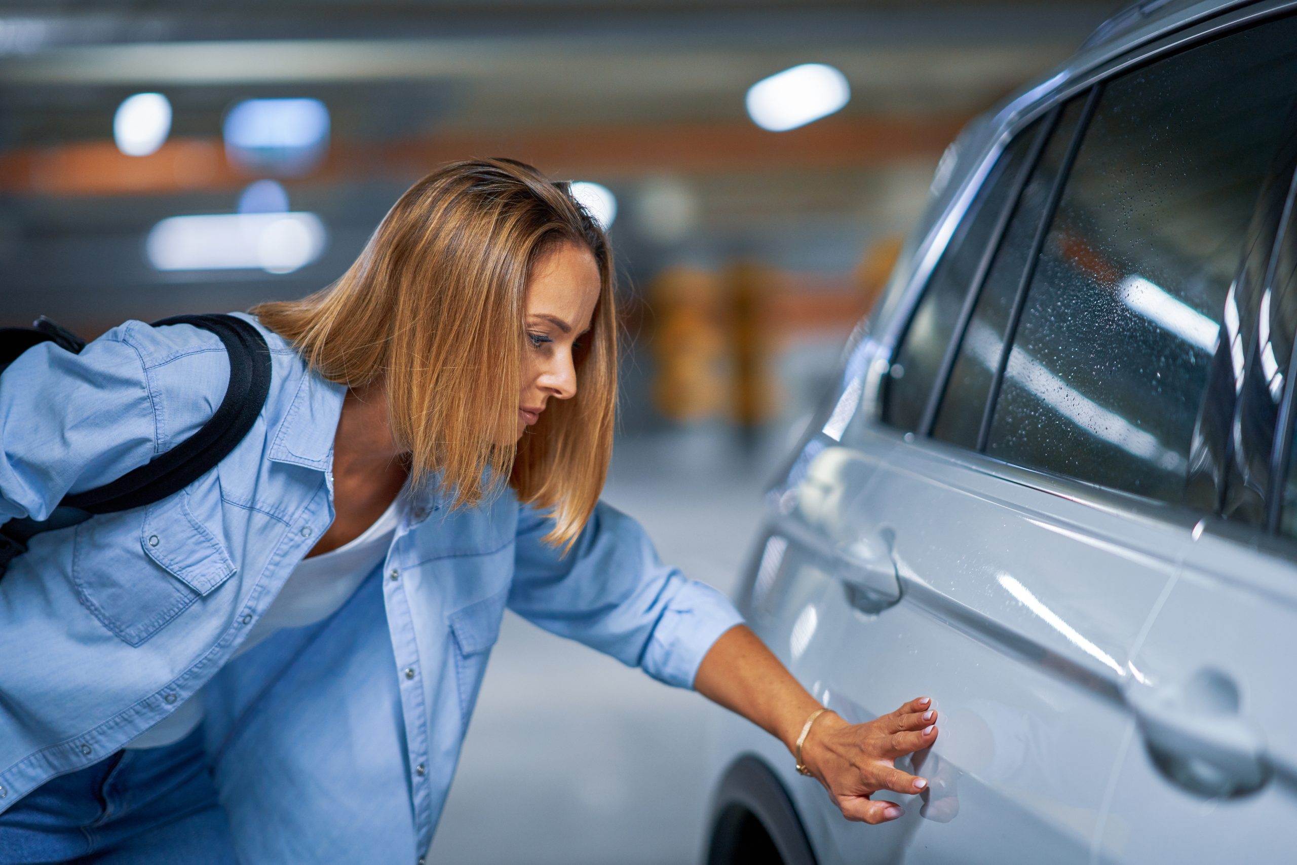 Portrait of young woman with scratched car at underground parking lot